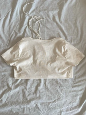 Vit croppad topp  - En vit croppad topp med korta ärmar. Man kan välja själv vilket håll man har toppen. Antingen som en croppad T-shirt med öppen rygg och snörning där bak. Eller med snörning på framsidan med djup U-ringning.