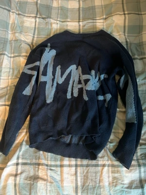 Mörkblå stickad tröja med tryck - Mörkblå stickad tröja med ljusgrått grafiskt tryck över ryggen. Tröjan har rund halsringning och långa ärmar. Perfekt för dig som gillar streetstyle och vill ha något unikt i garderoben.