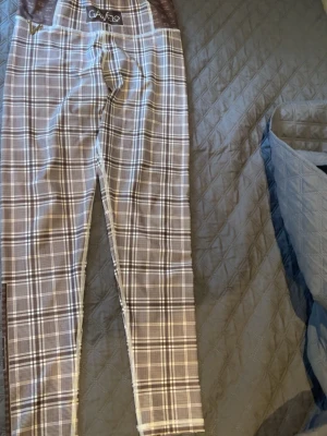 Rutiga leggings från Gavelo - Snygga leggings från Gavelo med rutigt mönster i svart, vitt och grått. De har hög midja och smal passform som sitter tight längs benen. Perfekta för dig som gillar trendiga och bekväma plagg med lite edge.