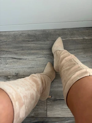 Beige knähöga boots med klack - Bara använda 1 gång!Säljer ett par snygga beige knähöga boots med spetsig tå och smal klack. Bootsens material är mjukt och ser ut som mocka, vilket ger en lyxig känsla. Perfekta för att lyfta vilken outfit som helst och ger en trendig vibe.