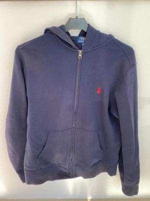 Mörkblå hoodie från Polo Ralph Lauren - Mörkblå hoodie med dragkedja från Polo Ralph Lauren. Tröjan är i fint skick, och är i storlek 160