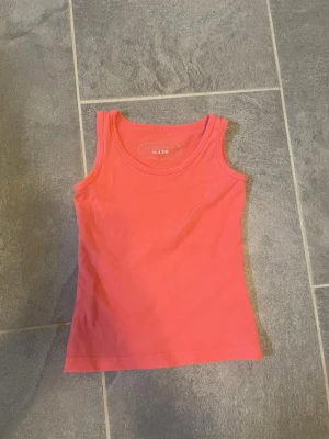 Rosa linne från Mywear Kids - Säljer ett enkelt och snyggt rosa linne från Mywear Kids. Linnet är ärmlöst med rund halsringning och tillverkat i mjukt bomullstyg. Perfekt att matcha med jeans eller shorts för en avslappnad look.
