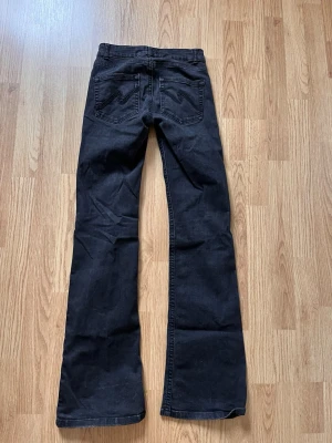 Svarta bootcut jeans med broderade fickor - Säljer ett par svarta bootcut jeans med snygga broderade detaljer på bakfickorna. Jeansen har klassisk femficksmodell, normal midja och utsvängda ben. Perfekta för dig som gillar en retroinspirerad look och vill ha ett par jeans som sticker ut lite extra.