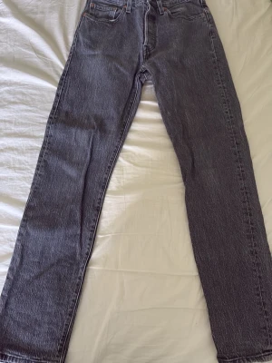 Svarta raka jeans med hög midja - Snygga svarta Levis 501 jeans med rak passform och hög midja. Klassisk femficksmodell och tydliga sömmar. Jeansen har en cool vintagekänsla och är perfekta till en avslappnad stil. Materialet är kraftig denim i bomull.