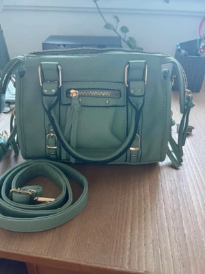 Mintgrön handväska med axelrem - Snygg mintgrön handväska i konstläder med guldfärgade detaljer. Väskan har både handtag och avtagbar axelrem, samt en liten ficka med dragkedja framtill. Perfekt storlek för det viktigaste och ger en fräsch touch till din outfit. Köpt på en marknad i Spanien 