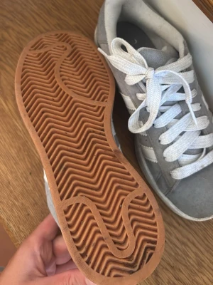 Gråa Addidas campus - Snygga sneakers, gråa med klassiska vita ränder på sidorna och vita skosnören. Yttersulan är i gummi med fiskbensmönster för bra grepp. Perfekta för dig som gillar en clean och sportig look.