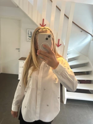 Vit skjorta med pärldetaljer från Zara - Säljer en vit skjorta från Zara med glittriga, silvriga pärldetaljer över hela skjortan. Skjortan har klassisk krage, lång ärm och bröstficka. Tillverkad i bomull och stängs med knappar framtill. Har aldrig använt, men saknar prislapp. Perfekt för dig som vill ha något extra till din outfit. 