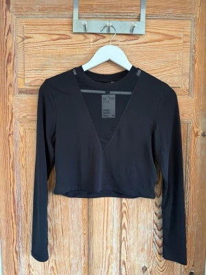 Svart croppad långärmad topp H&M - Snygg svart croppad topp från H&M med lång ärm och djup v-ringning med meshdetalj upptill. Perfekt för dig som gillar trendiga och stilrena plagg. Materialet är mjukt och stretchigt, vilket gör den bekväm att bära.
