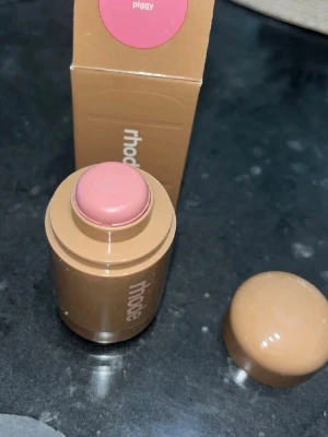 Rhode krämrouge i nyansen Piggy - Krämrouge från Rhode i en smidig stickform. Färgen heter Piggy och är en mjuk, ljusrosa ton som ger kinderna ett fräscht glow. Förpackningen är beige och kompakt, perfekt att ha med i väskan. Enkel att applicera direkt på huden för ett naturligt resultat.