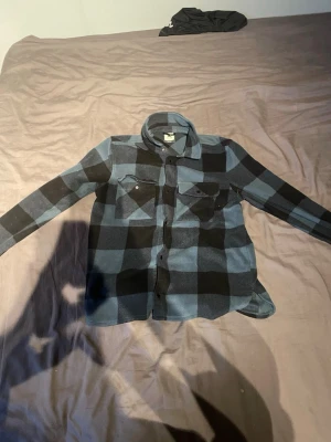 Blåsvart rutig overshirt McKinley - Säljer en blåsvart rutig overshirt från McKinley i mjukt fleece-material. Skjortan har två bröstfickor med lock och knappar framtill. Perfekt lager-på-lager-plagg med klassisk krage och långa ärmar.