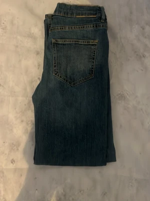 Blå raka jeans med bakficka - Säljer ett par klassiska blå jeans med rak passform och en enkel bakficka. Jeansen har en tidlös look och är sydda i ett robust denimtyg. Perfekta för dig som gillar en clean och enkel stil.