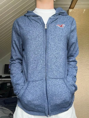 Blå hoodie från Hollister  - Säljer denna Hollister hoodien i storlek M. Modellen är 175 väger 65kg och har storlek S  Armlängd 68cm Bredd 48cm  Längd 63cm