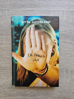 En farlig vän av Ritta Jacobsson - En ungdomsroman med färgstarkt omslag där en tjej håller upp handen med texten 'En farlig vän' skrivet på handflatan. Boken handlar om Leo och Jonna och teman som vänskap, kärlek och fara. Perfekt för dig som gillar spännande och realistiska berättelser.