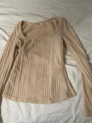 Beige ribbstickad tröja med rund hals - Säljer en beige ribbstickad tröja med lång ärm och bred, rundad halsringning. Tröjan har en figurnära passform och är tillverkad i ett mjukt, stretchigt material som känns skönt mot huden.