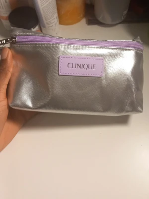 Clinique necessär  - Säljer ett set från Clinique med en metallic silver necessär med lila dragkedja. Perfekt för att förvara och ta bort smink.