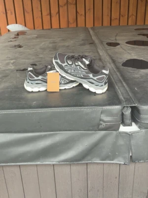 Svarta och grå Asics sneakers - Helt nya och oanvända Asics sneakers med tags kvar! 👟✨ Snygg modell i svart, grått och silver med skön GEL-dämpning. Passar lika bra till vardags som till träning och streetwear!  Märke: Asics  Skick: Helt nya / Oanvända med tag 🏷️  Färg: Svart / Grå / Silver  Storlek: 45  Tveka inte att skicka ett meddelande om du har några frågor eller vill ha fler bilder! Samfraktar gärna om du hittar något mer i min profil. 🚚✨
