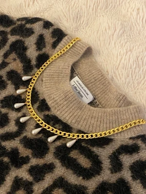 Guldhalsband med droppformade pärlor - Snyggt halsband i guldfärgad rostfritt med kedja och sex droppformade vita pärlor som hänger längs kedjan. Perfekt för att ge din outfit en trendig och elegant touch. Lätt att matcha med olika stilar och accessoarer.