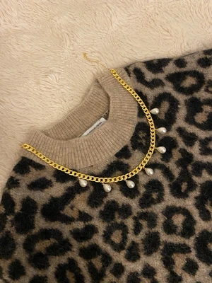 Guldkedja med pärldroppar - Snyggt halsband med en chunky guldfärgad kedja och hängande vita pärldroppar. Perfekt för att ge din outfit en trendig och elegant touch. Halsbandet har en klassisk design med moderna detaljer och passar till många olika stilar.
