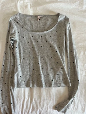 Grå långärmad topp från Nelly - Säljer en grå långärmad topp från Nelly med små svarta stjärnor över hela tyget. Toppen har en rundad, lite djupare urringning.