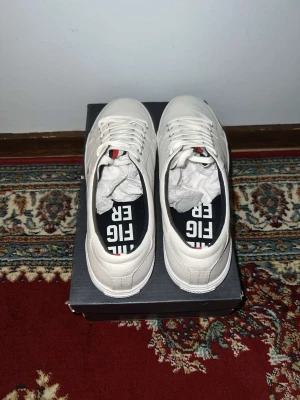 Vita sneakers från Tommy Hilfiger - Snygga vita sneakers från Tommy Hilfiger med klassisk låg profil och diskret logga på innersulan. Skorna har vita snören och ovandel i slätt material, perfekt för en clean och stilren look. Passar dig som gillar enkel och modern stil.