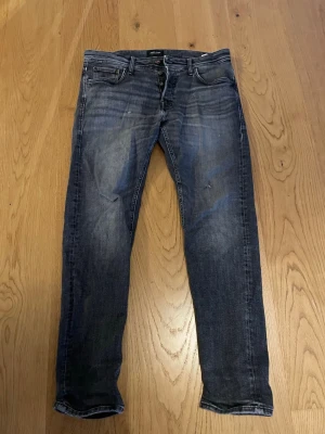 Jack and Jones taperd jeans  - Använda jeans som har hål nära dragkedjan och med hemmagjorda slitningar, annars fint skick dock lite urtvättade