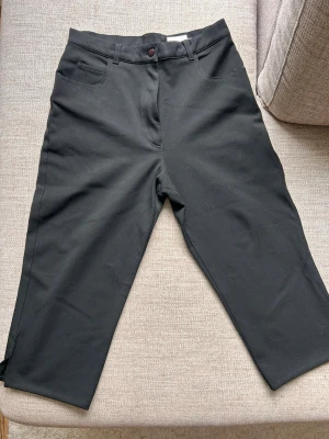 Svarta knälånga shorts Stl 38  - Snygga, svarta, knälånga shorts med midwaist passform och raka ben. Shortsen har bälteshällor, knapp och dragkedja framtill, sprund samt praktiska fickor. Perfekta för dig som gillar en enkel och stilren look. Stl 38