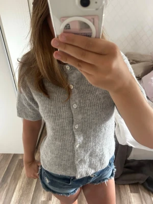Grå ribbad kortärmad kofta - Säljer en grå ribbad kofta med korta ärmar och knappar framtill. Den är från Gina tricot den är köpt i april så väldigt ny. 