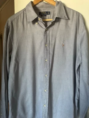 Grå skjorta från Polo Ralph Lauren XL - Klassisk grå skjorta från Polo Ralph Lauren i bomull. Skjortan har lång ärm, knappar framtill och den ikoniska broderade loggan på bröstet. Perfekt till jeans eller chinos för en clean och stilren look.