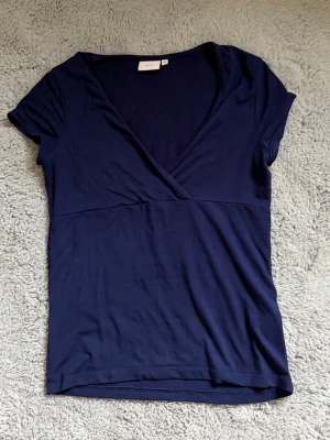 Mörkblå omlottopp med v-ringning - Snygg mörkblå topp med omlottdesign och djup v-ringning. Kortärmad och i mjukt, stretchigt material som sitter skönt på kroppen. Perfekt till jeans eller kjol för en clean look.