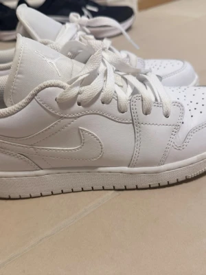 Vita Air Jordan 1 Low sneakers - Säljer ett par helvita Air Jordan 1 Low sneakers med klassisk swoosh på sidan och Jumpman-logga på plösen. Skorna har perforerad tå, vita skosnören och är tillverkade i läder. Perfekta för dig som gillar stilrena och tidlösa sneakers. De är köpte från zalando för 1099kr.