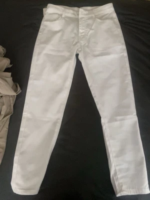 Vita raka jeans med hög midja - Säljer ett par vita jeans med rak passform och hög midja. Jeansen har klassiska fem fickor och stängs med dragkedja och knapp. Perfekta för en clean och fräsch look. Materialet känns mjukt och följsamt.
