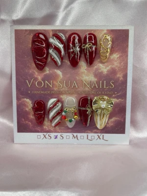RubyNoël (S);Medium Almond - Handgjorda press-on naglar i rött och vitt med glitterdetaljer, guldfärgade dekorationer och små pärlor. Mix av mönster som polkagris, rosetter och julinspirerade motiv. Medium långa , mandelformade naglar som ger en lyxig och unik look.S: 15 mm, 11,5 mm, 12 mm, 11 mm, 9 mm 