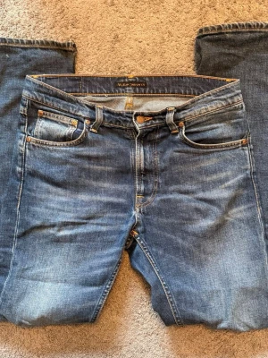  Nudie Jeans - Säljer ett par klassiska blå jeans från Nudie Jeans med orangea sömmar. Jeansen har en rak passform. modell: Lean Dean W30 L32
