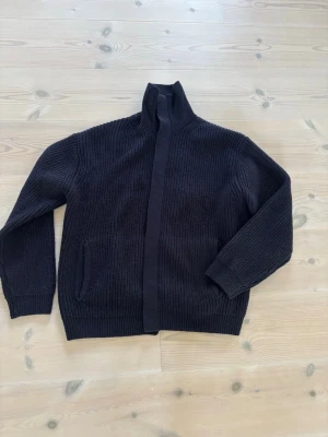 Mörkblå stickad cardigan Zara - Stickad kofta från Zara i mörkblå med hög krage och tryckknappar framtill. Grovstickad struktur och en ficka på ena sidan. Perfekt för lager på lager och enkel att matcha med olika outfits.