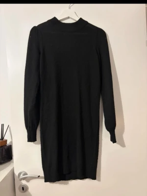 Svart stickad långärmad klänning - En svart stickad klänning med lång ärm. Klänningen har en rak passform och slutar strax ovanför knäna. Perfekt för kyligare dagar och enkel att styla med accessoarer.