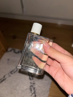 Burberry her parfym med vit kork - Stilren parfym från Burberry i en genomskinlig, rektangulär glasflaska med vit kork och gulddetalj. Flaskan har Burberry-loggan ingraverad framtill och innehållet är ljust gult. Perfekt för dig som gillar klassisk och elegant design. bra för vinter och vår. kom gärna med bud och frågor ❤️❤️ köpt för 1499kr men inte min smak så därför priset, kolla gärna på min profil för mer parfym och bra rabatt på bundels