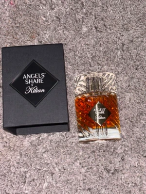 Angels' Share parfym från Kilian - Exklusiv parfym från Kilian, Angels' Share, i en elegant genomskinlig glasflaska med kristalliknande detaljer och bärnstensfärgad vätska. Medföljer en svart lyxig förpackning med diamantformat märke på framsidan.