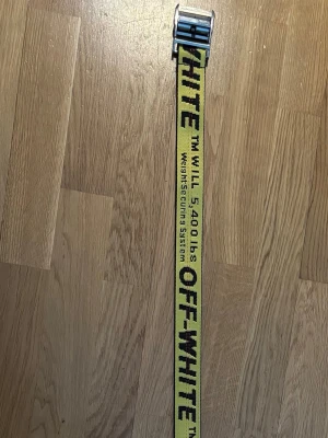 Off-White Industrial Belt Gul  - Detta är ett äkta Off-White Industrial Belt i en klar gul färg med svart logotyp och röda sömnadsdetaljer. Den ikoniska designen kännetecknas av texten "™ WILL 5,400 lbs Weight Securing System" som upprepas längs bandet, kompletterat med ett silverfärgat metallspänne med präglad text: "OFF-White™" och "BELT". ⭐️ Skick: 7/10 (Mindre repor och slitage på spännet) 🎲 Storlek: 129 cm 🎨 Färg: Gul och svart 📦 Snabb och omsorgsfull frakt