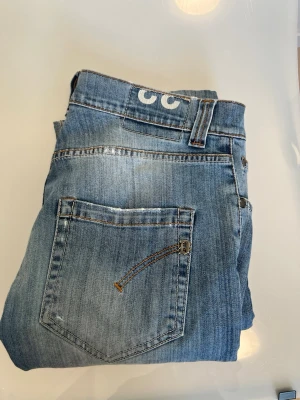 Blåa dondup jeans  - W 33 l33Säljer ett par ljusblå dondup  jeans med raka ben och klassisk femficksdesign. Jeansen har slitningar och kontrastsömmar samt en unik broderad detalj på bakfickan. Passar perfekt till en avslappnad streetwear-look.
