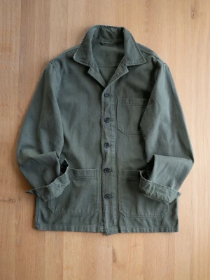 Olivgrön overshirt med fickor - Stilren olivgrön overshirt i kraftigt bomullstyg med tre utanpåliggande fickor och knappar framtill. Klassisk krage och raka ärmar. Perfekt lager-på-lager-plagg för en avslappnad look.