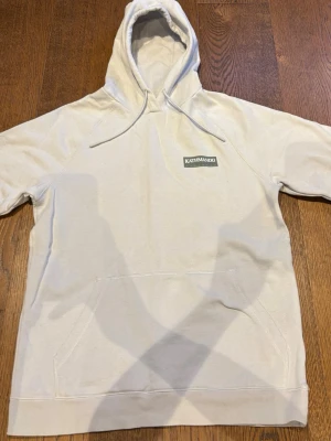 Beige hoodie från Kathmandu - Snygg beige hoodie från Kathmandu med stor logga på ryggen och mindre logga på bröstet. Klassisk känguruficka framtill och justerbar huva med dragsko. Perfekt för chill dagar och enkel att matcha med jeans eller joggers. Köpt i Nya Zeeland för 1099 kr och är använd 1-2 gånger! Hör av dig vid fler frågor!