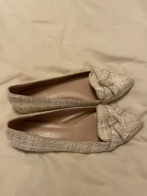 ballerinaskor med rosett - Snygga ballerinaskor från Ann Taylor i beige tweedliknande tyg. Skorna har spetsig tå och en dekorativ rosett framtill. Bekväm innersula i ljusrosa nyans. De står storlek 38 men skulle mer säga att de upplevs som en 37