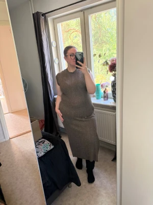 Brun ribbad ärmlös långklänning - Säljer en guld, ribbad långklänning med ärmlös design och rund hals. Klänningen har en kroppsnära passform och är stickad i ett mjukt material som ger en snygg siluett. Perfekt för dig som gillar stilrena och bekväma plagg. Från märket Odd Molly i storlek 2 som enligt deras storlekguide motsvarar en storlek M. Jag har vanligtvis en 4/XL. Passar en L. Mycket fint skick, jag hittar inga synliga anmärkningar eller defekter.  