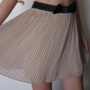 Vippig Ljus Sommarkjol Forever21 Svart Rosett Midja - Söt plisserad kjol med svart rosett i midjan. Fint skick. Modellen på bilden är ca 168 cm lång och har 34/36