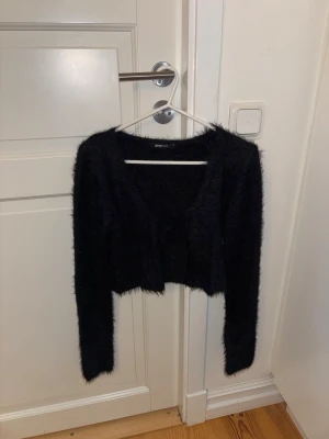 Svart fluffig kofta från Gina Tricot - Säljer en svart, fluffig och croppad kofta från Gina Tricot. Koftan har långa ärmar och en mjuk, lurvig textur som ger en trendig look. Perfekt att slänga över en topp för en cool och mysig stil. en kofta som man knyter, skitsnygg ❤️❤️