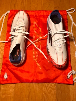 Adidas F50 Pro / F50+ FG – storlek 42 - Säljer ett par Adidas F50 fotbollsskor i färgen vit/solar red/lucid blue. Storlek 42. Skorna är i perfekt/nyskick – har knappt använts (eller inte alls). Originalbox och skopåse medföljer. Har Lightstrike Pro i sulan. Superlätt och snabb modell, perfekt för den som vill ha max acceleration. Pris: 1 200 kr (kan diskuteras vid snabb affär)