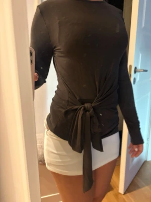 Svart långärmad topp med knyt - Snygg grön långärmad topp med rund hals och knyt i midjan som ger en cool och trendig look. Toppen har en slim passform och är perfekt att styla med kjol eller jeans. Materialet känns mjukt och följsamt.