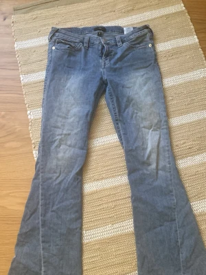 Blå true religion bootcut jeans - Snygga blå bootcut jeans med klassiska fem fickor och dekorativa sömmar på bakfickorna. Jeansen har knappar och dragkedja framtill samt vita detaljer på fickorna. Tillverkade i denim med lätt tvättad look.