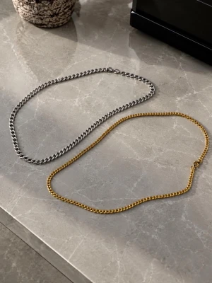 Två kedjehalsband i guld och silver - Säljer två stilrena halsband i kedjemodell, ett i guldfärg och ett i silverfärg. Båda har klassisk, platt länkkedja och enkel låsning. Perfekta för att kombinera eller bära var för sig för en trendig look.