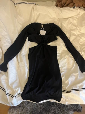 Svart långärmad cut out klänning - Trendig svart klänning från C.W. med lång ärm och snygg cut out-detalj framtill. Klänningen har en tight passform och är perfekt för dig som vill sticka ut. Materialet känns mjukt och följsamt mot kroppen.